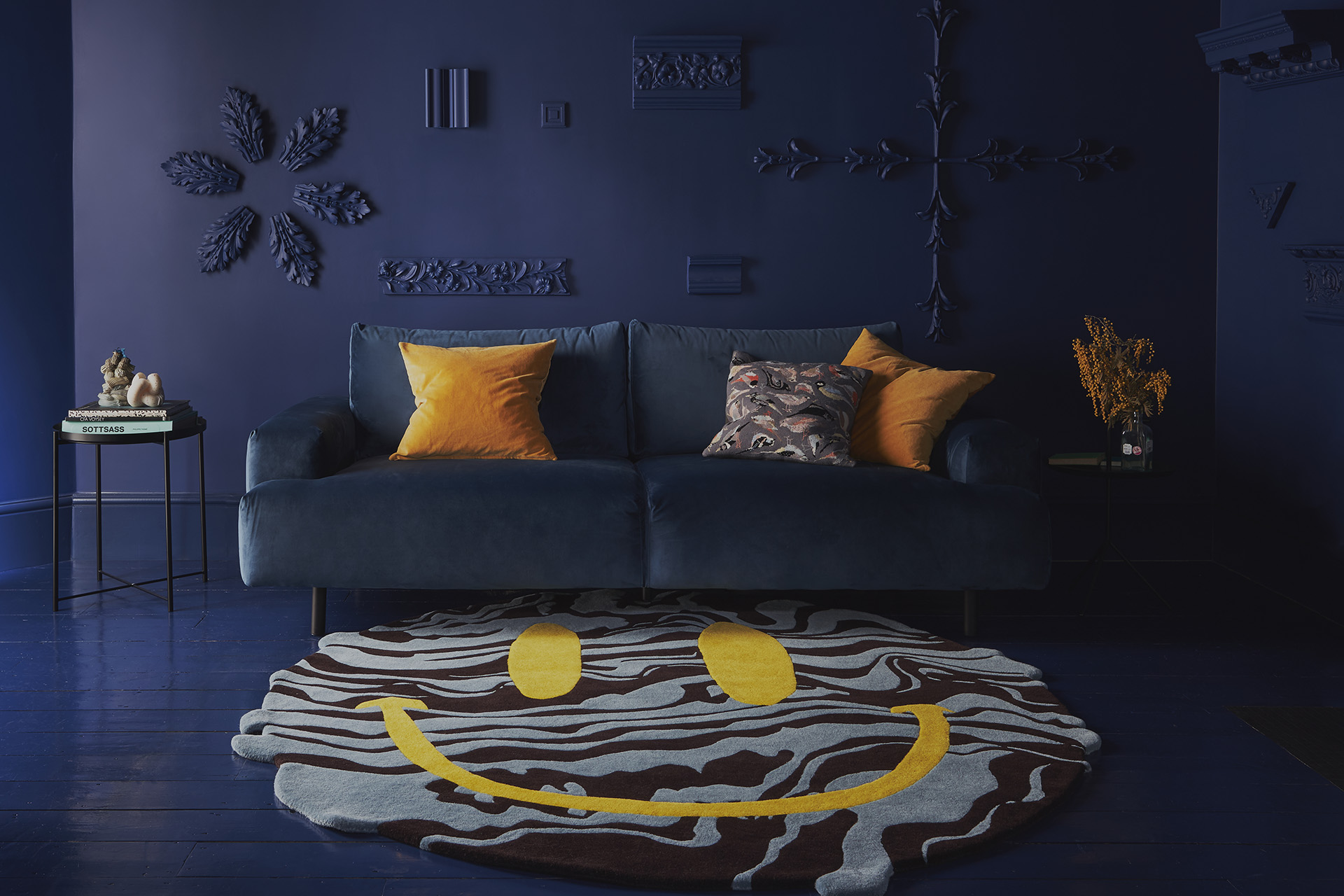 Room with dark blue walls and sofa featuring a large rug with yellow smiley face