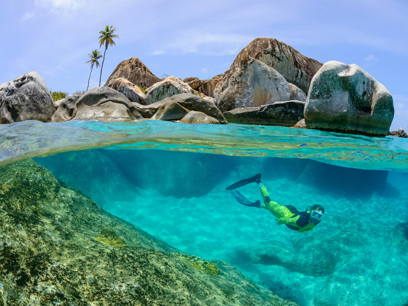 Snorkeler underwater in front of large granite boulders