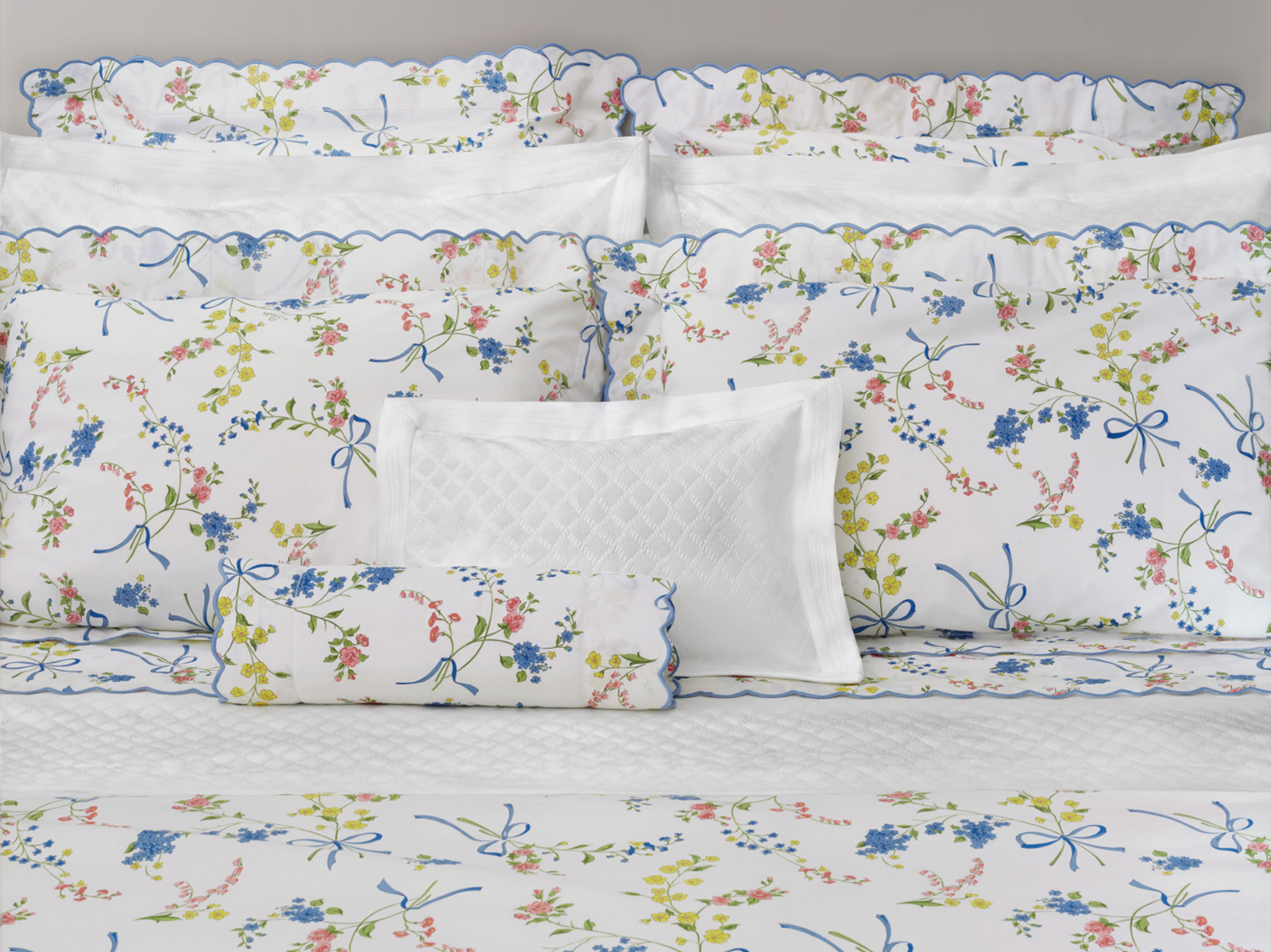 Close up of pillows on a bed made with floral patterned linens on a white background