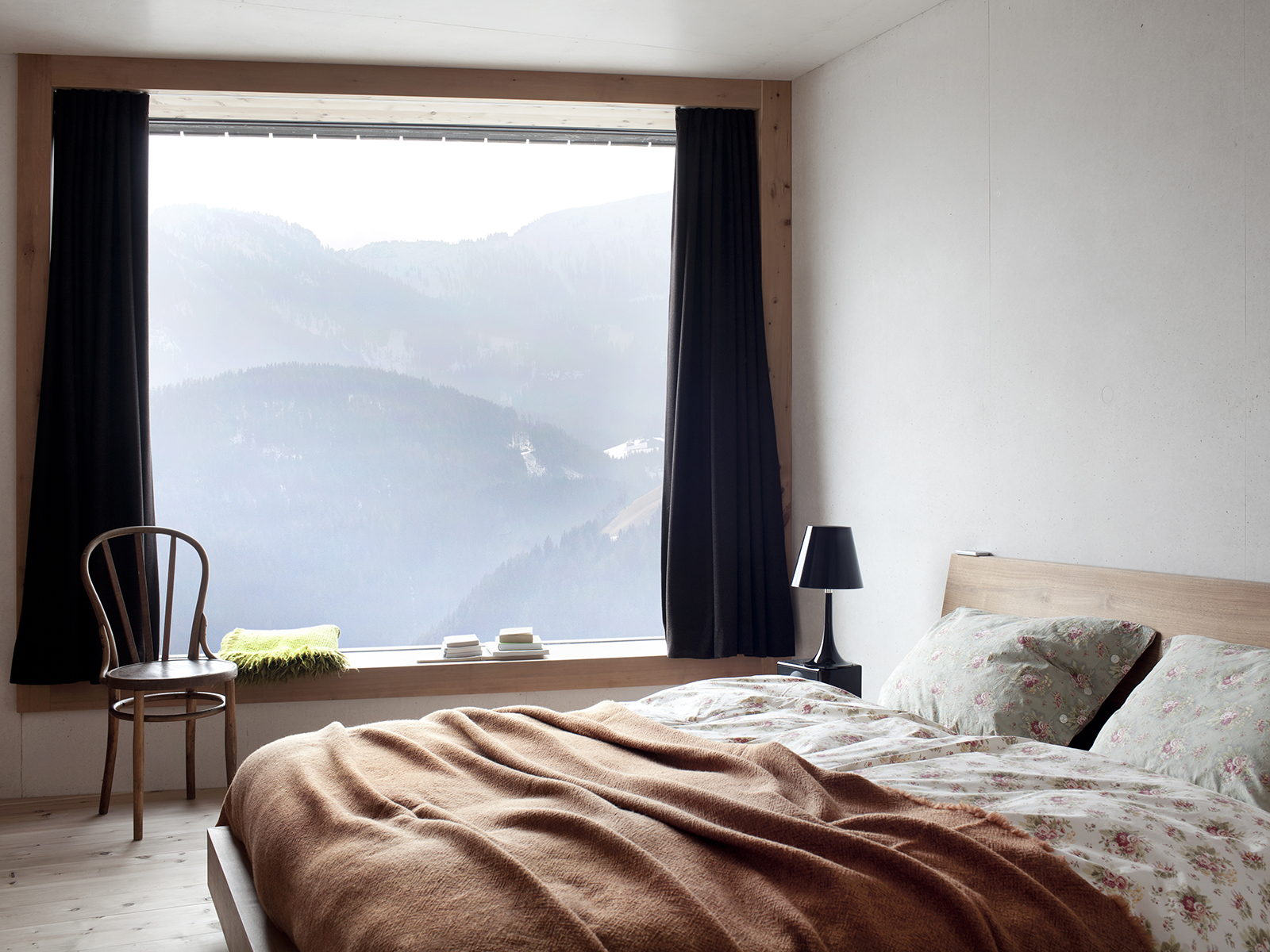 Simple room featuring double bed, chair, light, and window with stunning views across the mountains
