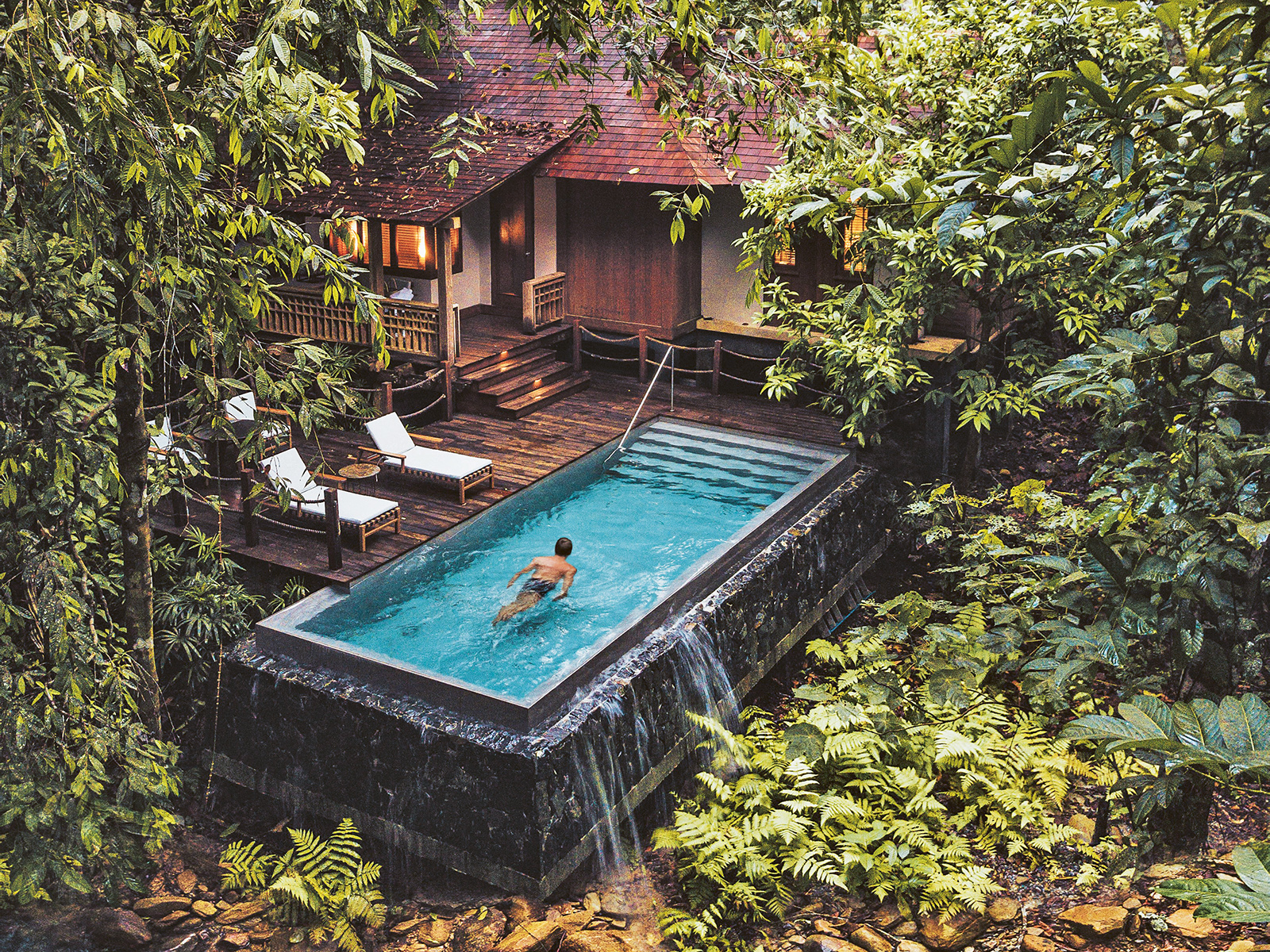 A villa with sun loungers and pool set in the lush green rainforest