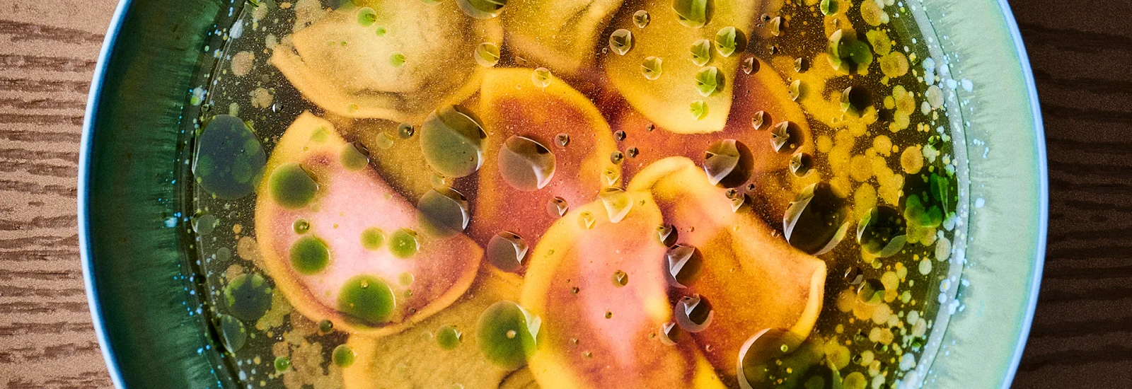 Ravioli in a green bowl on a wooden table, photographed from above